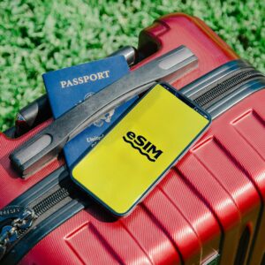 Close-up of a red suitcase with a smartphone displaying eSIM and a passport, symbolizing travel readiness.