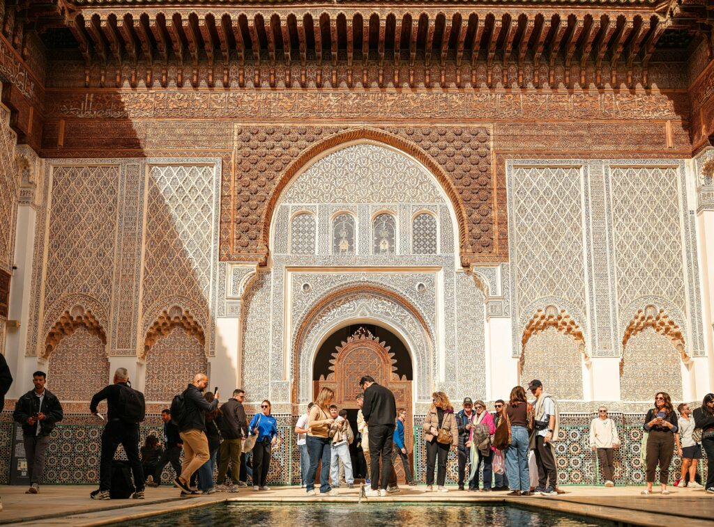 Group of tourists exploring Ben Youssef Madrasa's intricate architecture in sunny Marrakech.